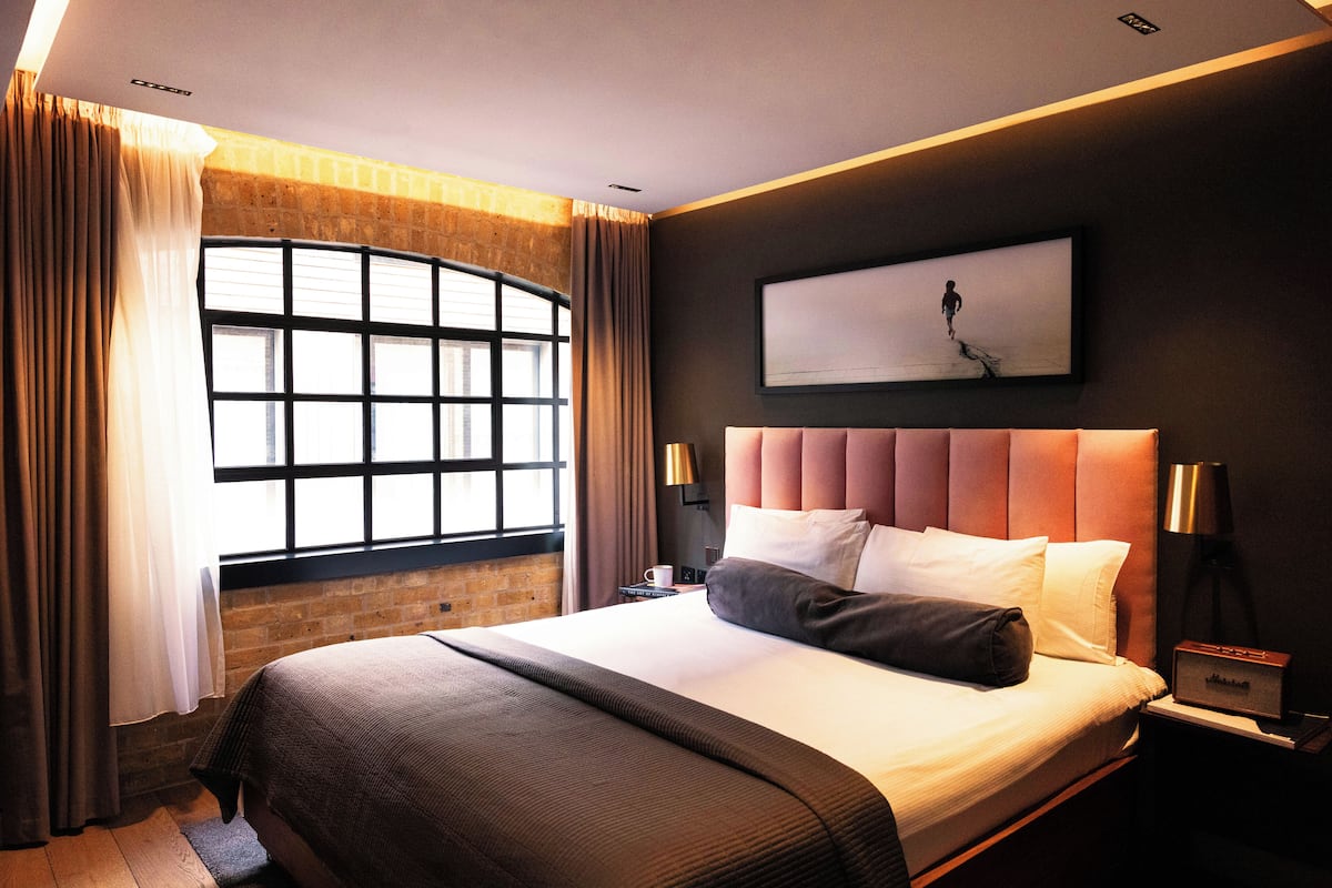 Quarto de hotel moderno com uma cama grande, vista da cidade pela janela e um quadro na parede.