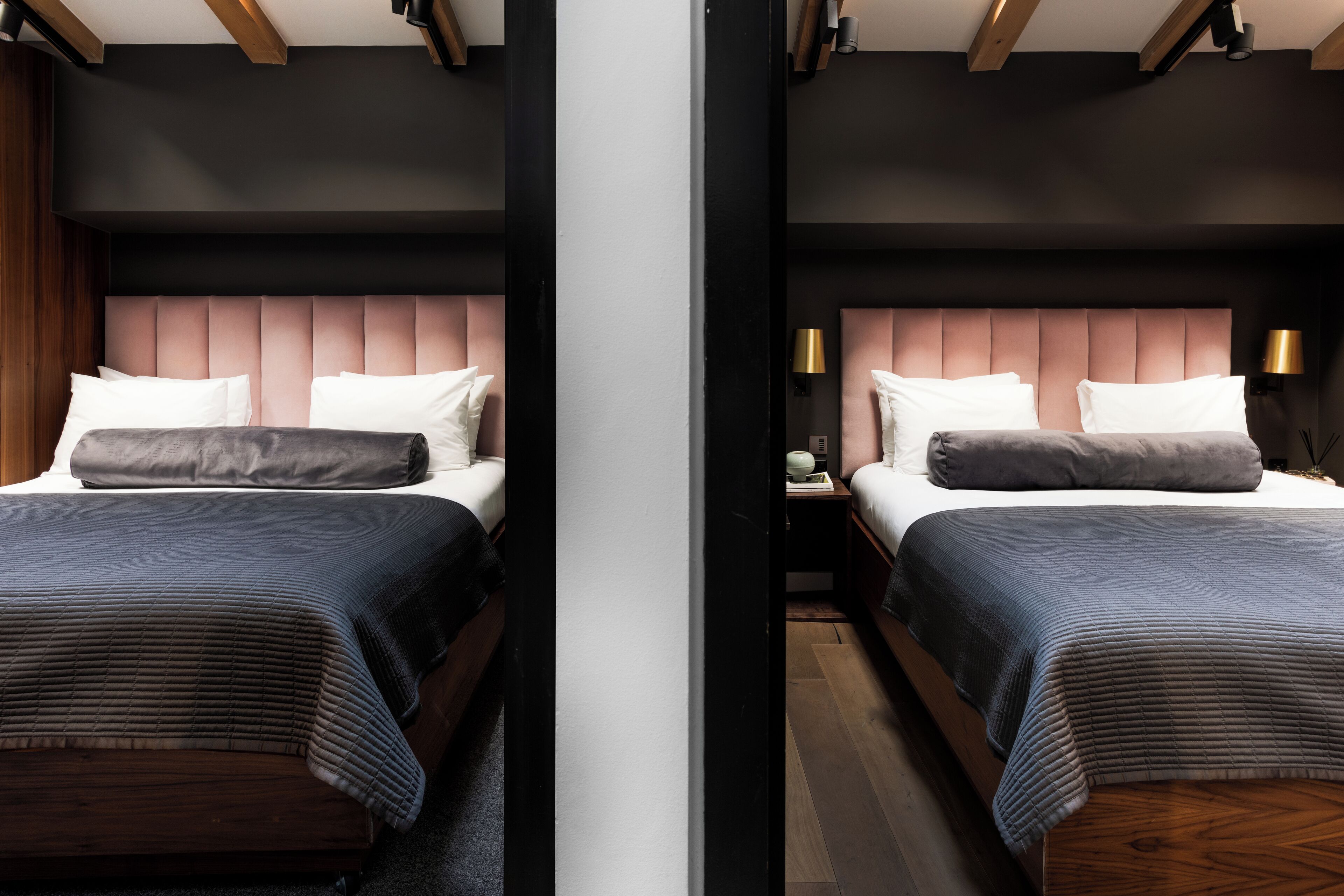 A modern hotel room with two beds, each with a wooden headboard, a dark-colored bedspread, and a bedside lamp.