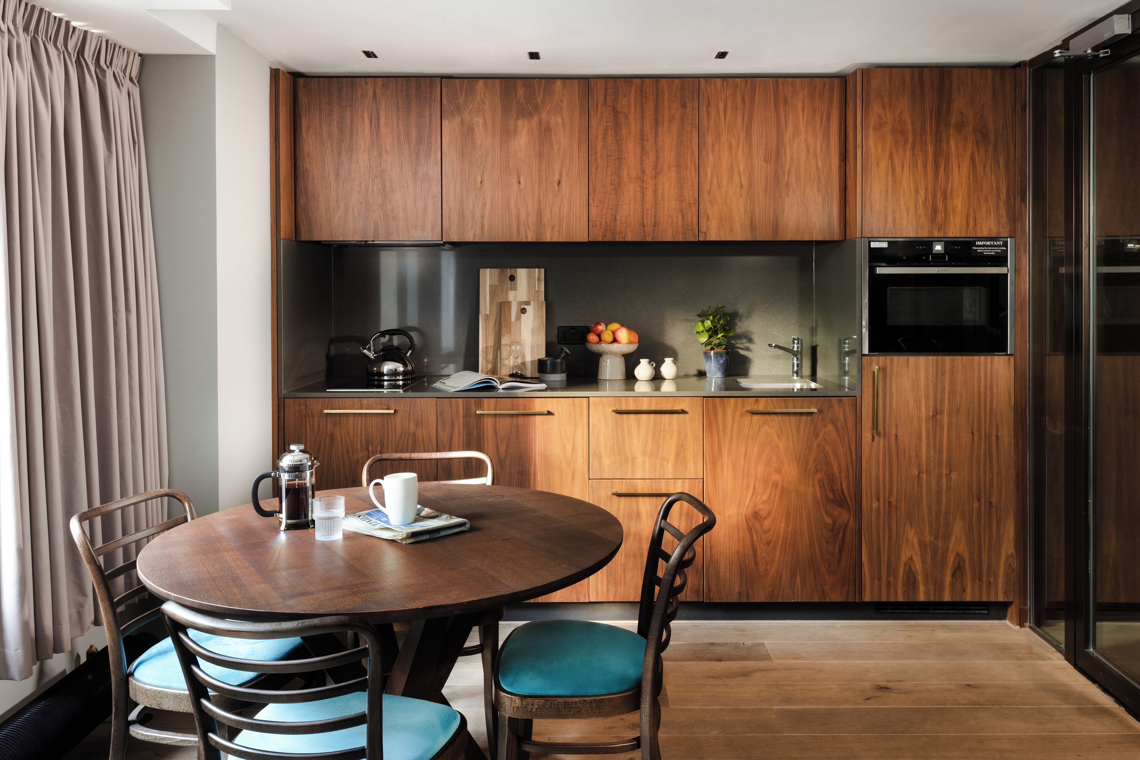 Une cuisine moderne avec des meubles en bois, une table de salle à manger ronde entourée de chaises et un four encastré.