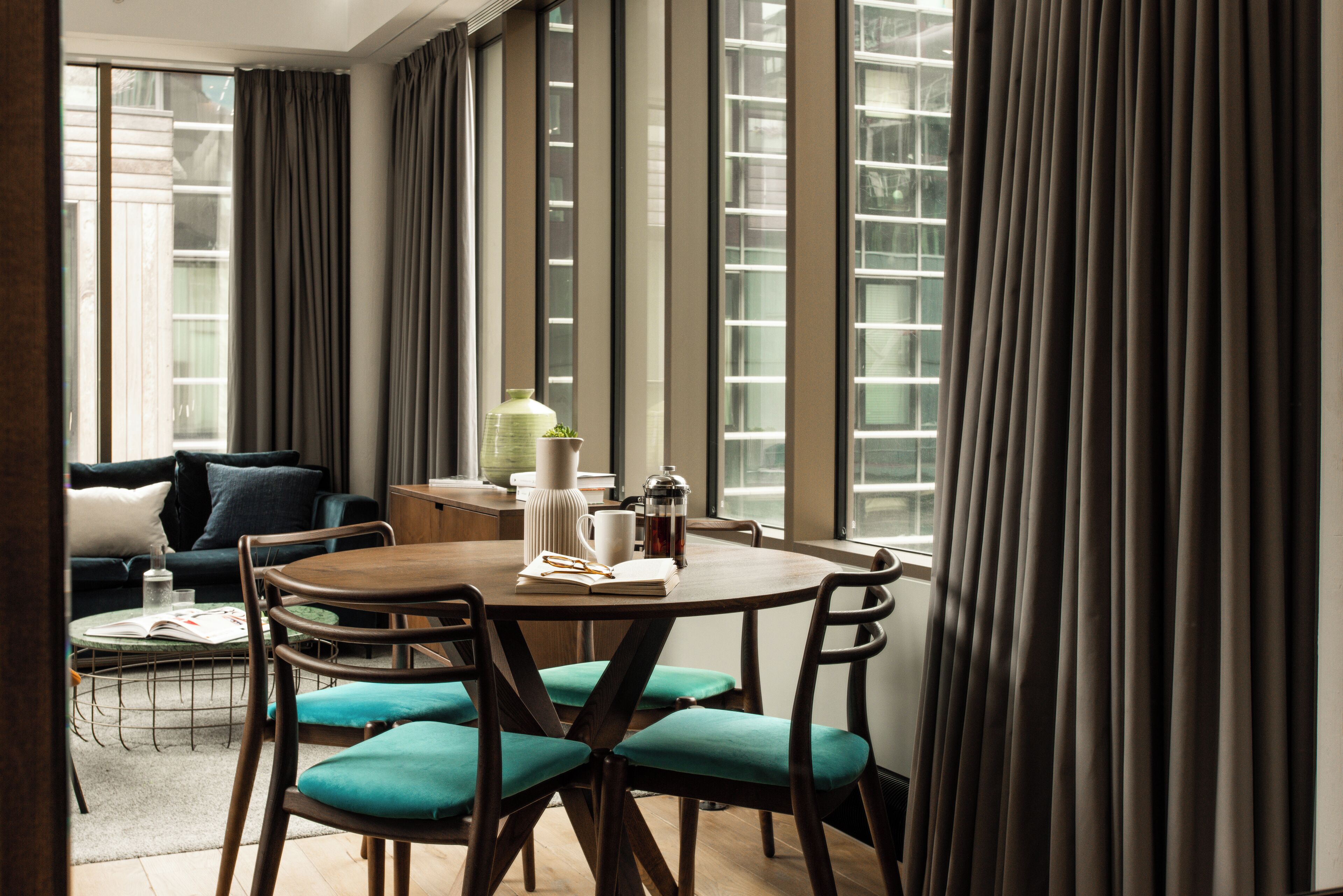 Un espace de salle à manger moderne avec une table ronde, des chaises et une vue sur la ville grâce à de grandes fenêtres.