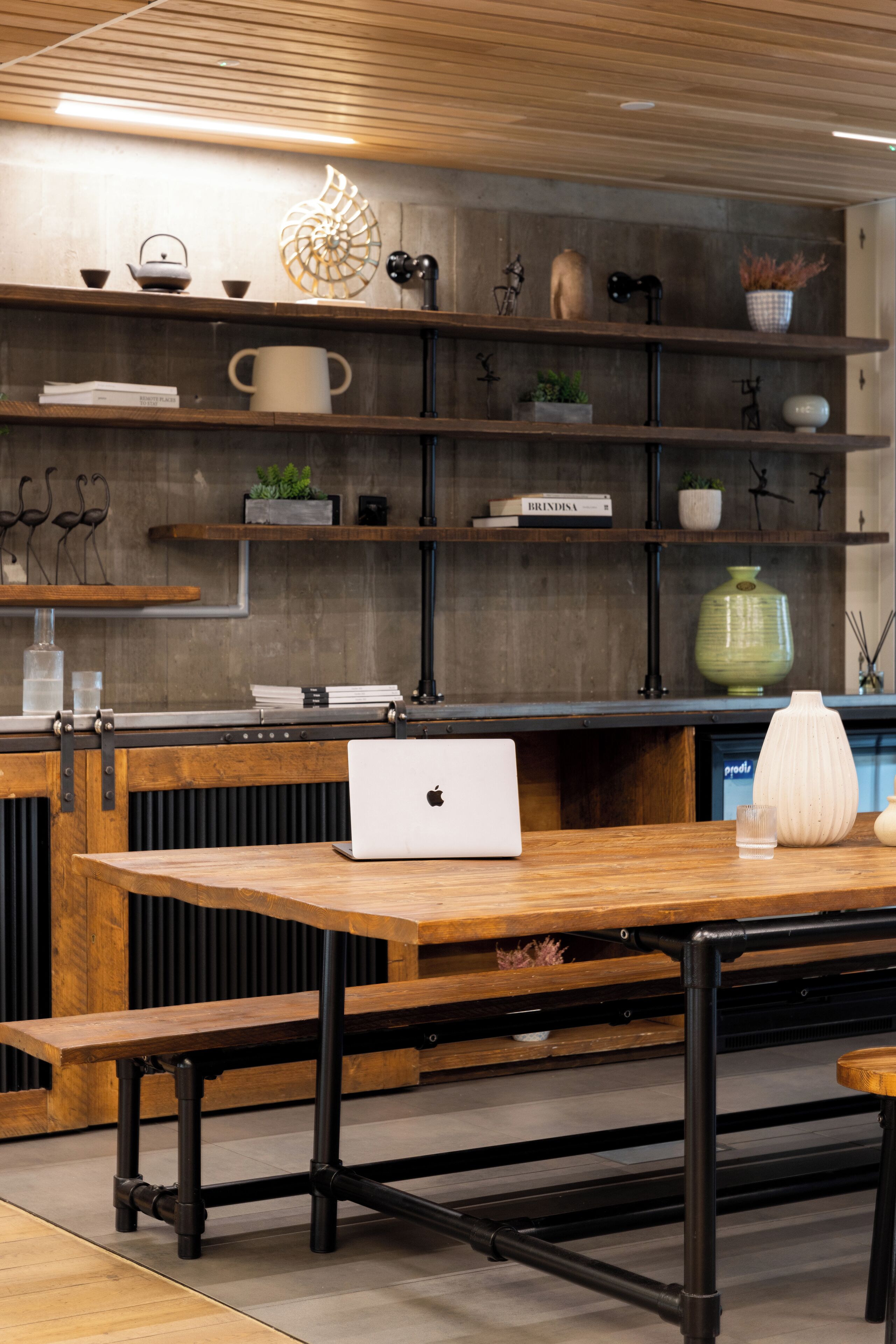 A modern kitchen with wooden shelves, a laptop on a wooden table, and various kitchen items.