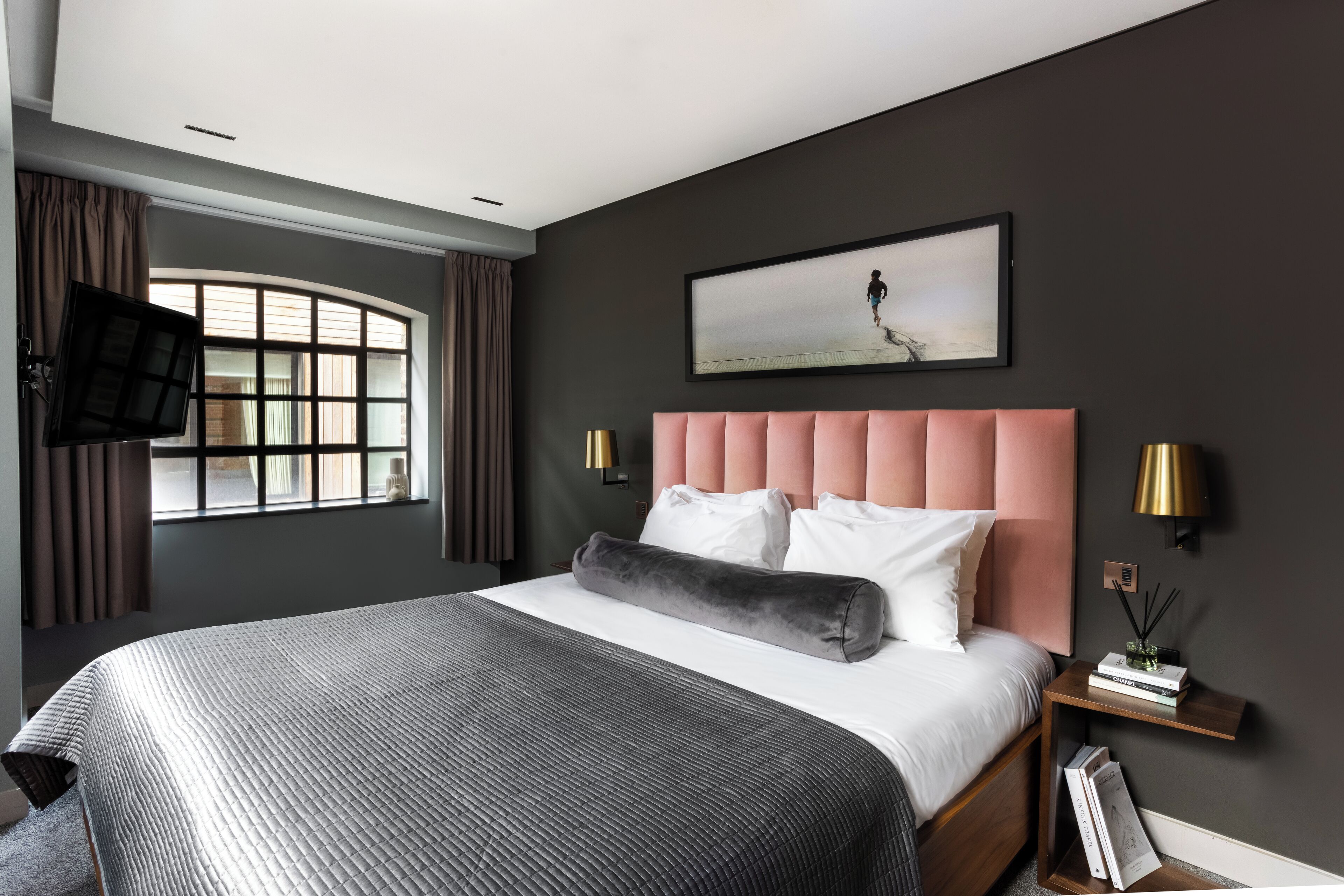 Quarto moderno com uma cama grande, televisão na parede e janela com cortinas.