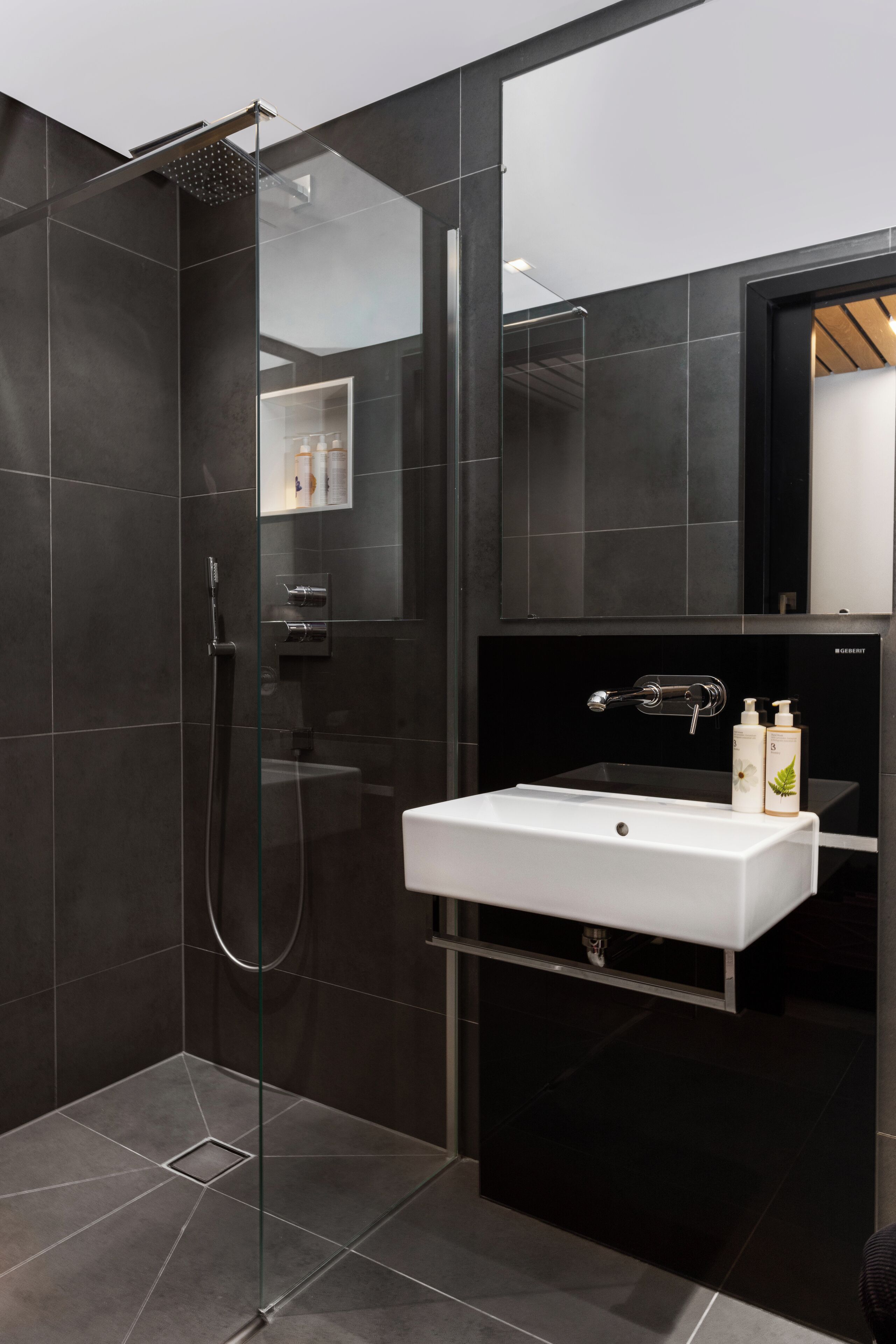 Een moderne badkamer met een douchecabine van glas, een witte wastafel en een spiegel erboven.