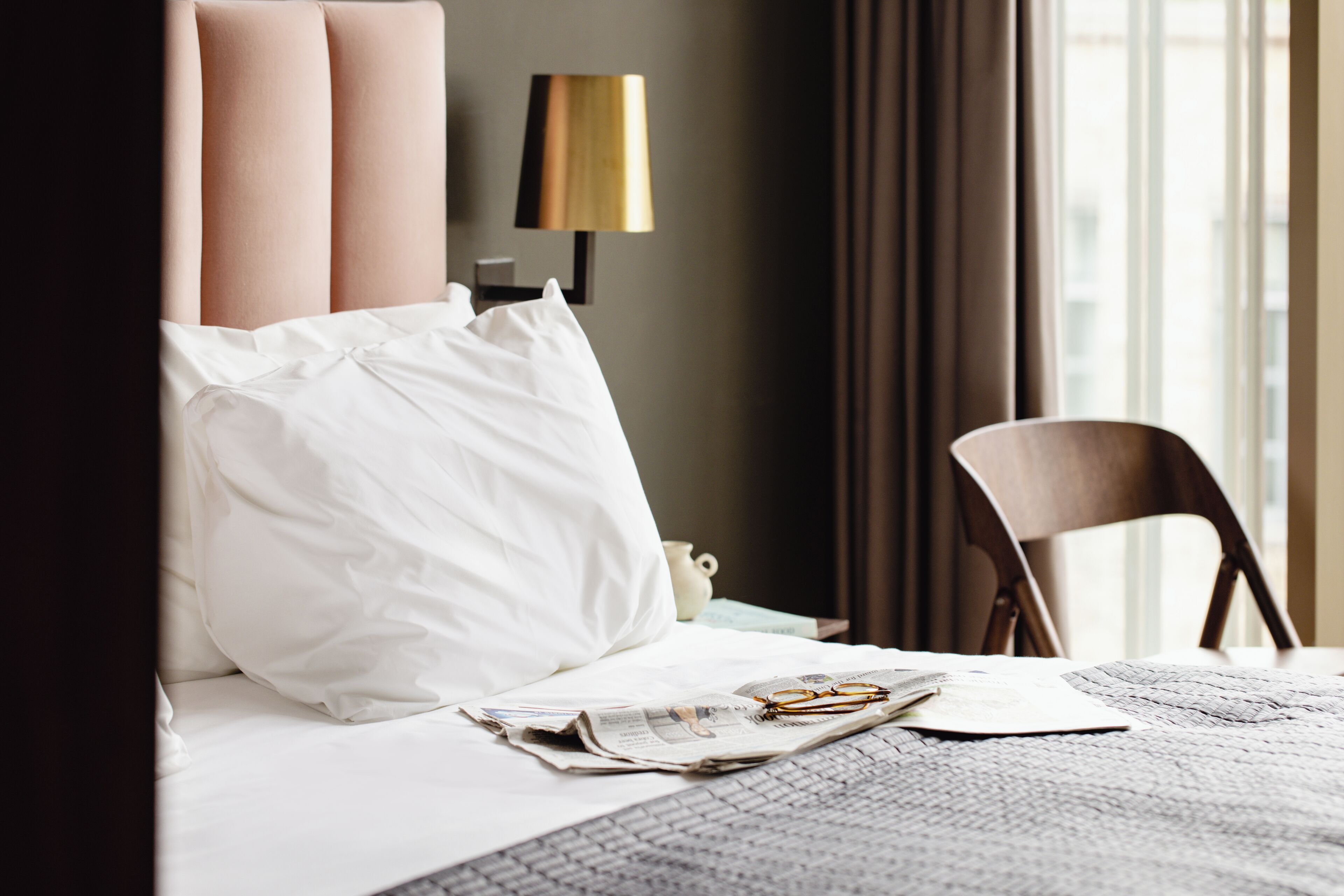 Un lit bien fait, avec des draps blancs, une paire de lunettes et un journal posés sur le lit.
