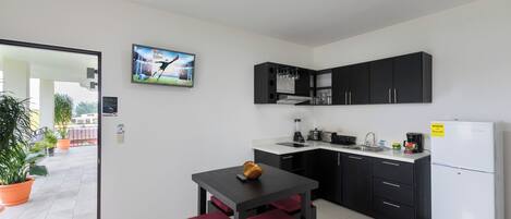 A compact kitchen with a dining area, a refrigerator, and a television displaying a sports event.