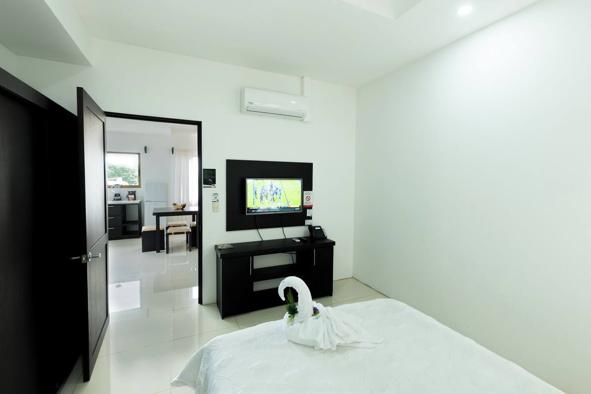 A hotel room with a bed, a TV, a desk, and a door.