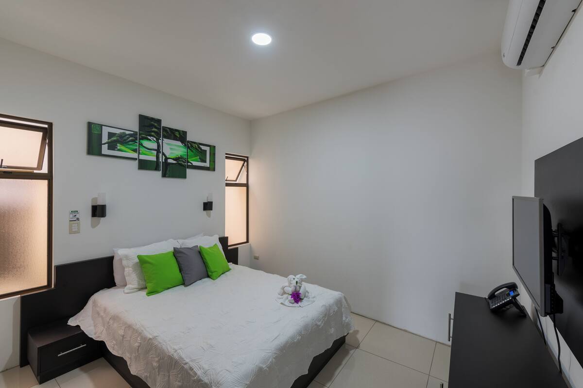 A modern hotel room with a bed, a desk with a phone, and a TV.
