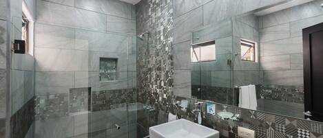 A modern bathroom with a large mirror, a glass-enclosed shower, and a white sink.