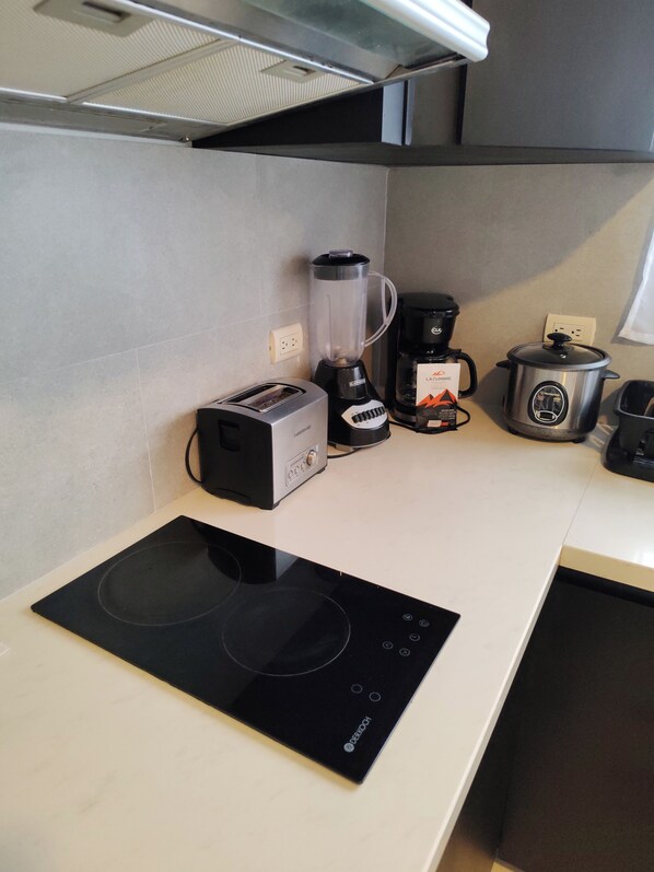 A kitchen with a black induction cooktop, a toaster, a blender, a coffee maker, and a slow cooker. - La Casona (La Fortuna)
