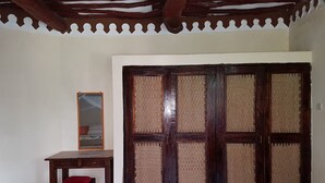 A room with a large wooden door, a small wooden table with a red cushion, and a mirror on the wall. - Kivuli Villas (Diani Beach)