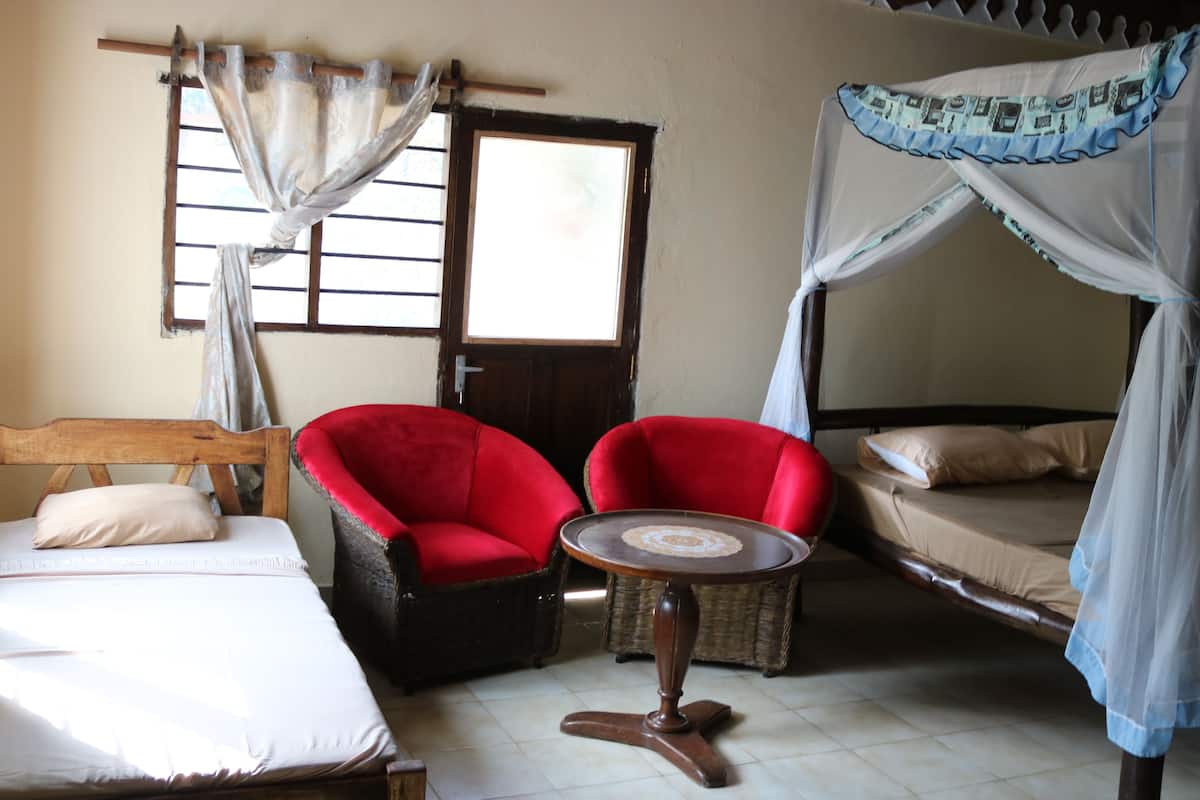A room with a bed, two red chairs, a small table, a window with curtains, and a mosquito net over the bed.