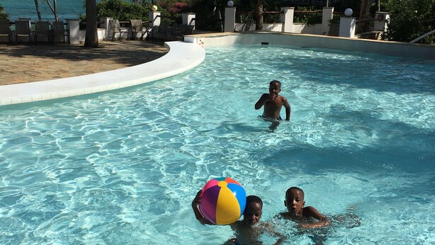 A swimming pool with clear blue water, surrounded by lounge chairs and palm trees. - Kivuli Villas (Diani Beach)