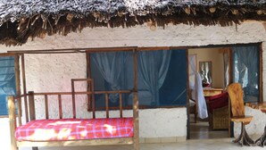 A room with a wooden bed, a chair, and a small table. - Kivuli Villas (Diani Beach)
