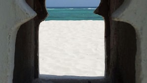 A doorway leading to a beach with a clear view of the ocean and sandy shore. - Kivuli Villas (Diani Beach)