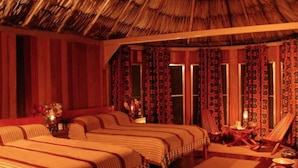 Una habitación con dos camas, techo de paja y cortinas estampadas.