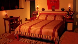 Una habitación tradicional con cama, dos mesitas de noche, una silla y un ventanal con cortinas.