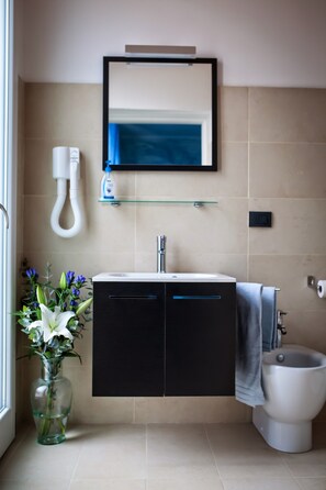 A bathroom with a black vanity, a white toilet, a glass shelf with toiletries, and a vase with flowers. - La Maison di Luca (Verona)