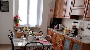 A kitchen with wooden cabinets, a granite countertop, a dining table with chairs, and a window with curtains. - La Maison di Luca (Verona)