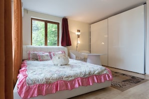 Un dormitorio con cama, mesita de noche, una silla, armario y ventana con cortinas.