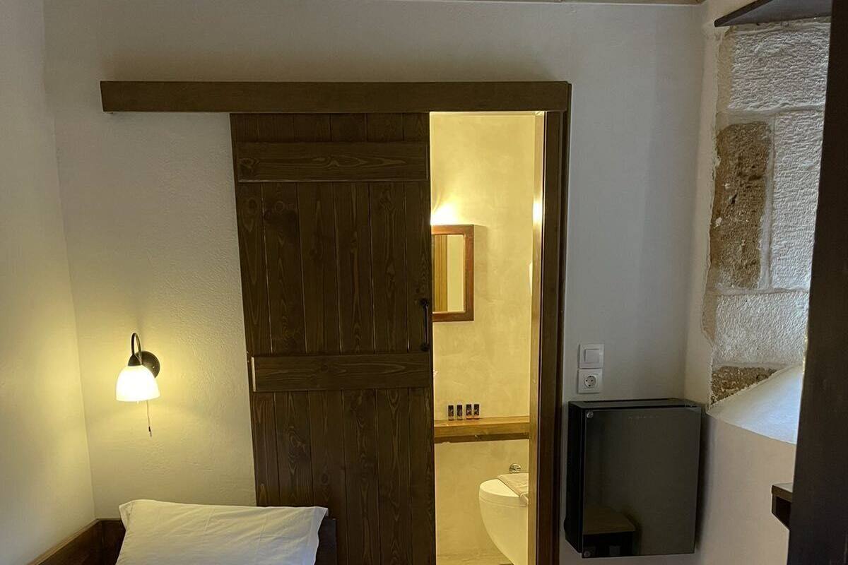 Un dormitorio con cama, armario de madera, televisor y baño visible a través de una puerta abierta.