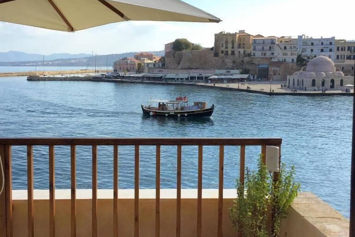 Un balcón con vista a una masa de agua, un barco y edificios al fondo.