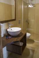 A bathroom with a white sink, a mirror, a wooden vanity, a glass shower enclosure, and a toilet.