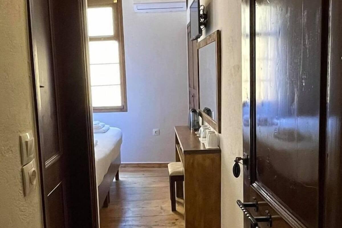 Un pasillo estrecho que conduce a un dormitorio con cama, una mesita y un espejo.