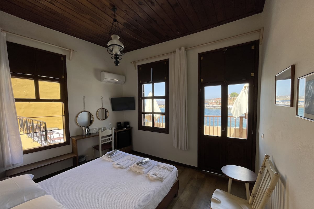 Una habitación con cama, escritorio, silla, televisor y ventana con vista al mar.