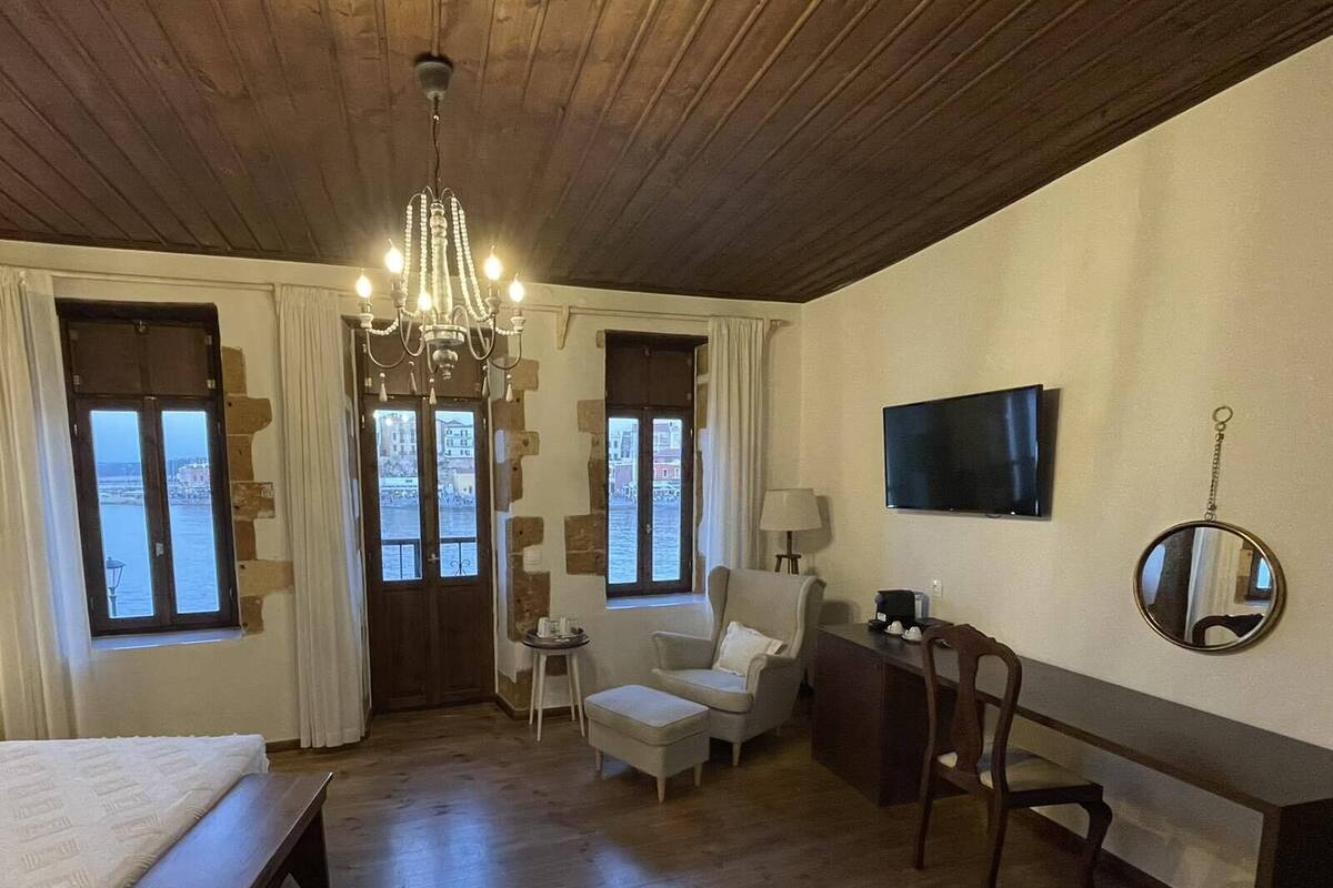 Habitación de hotel con techo de madera, una cama, un escritorio, una silla, un televisor y dos ventanas con cortinas.