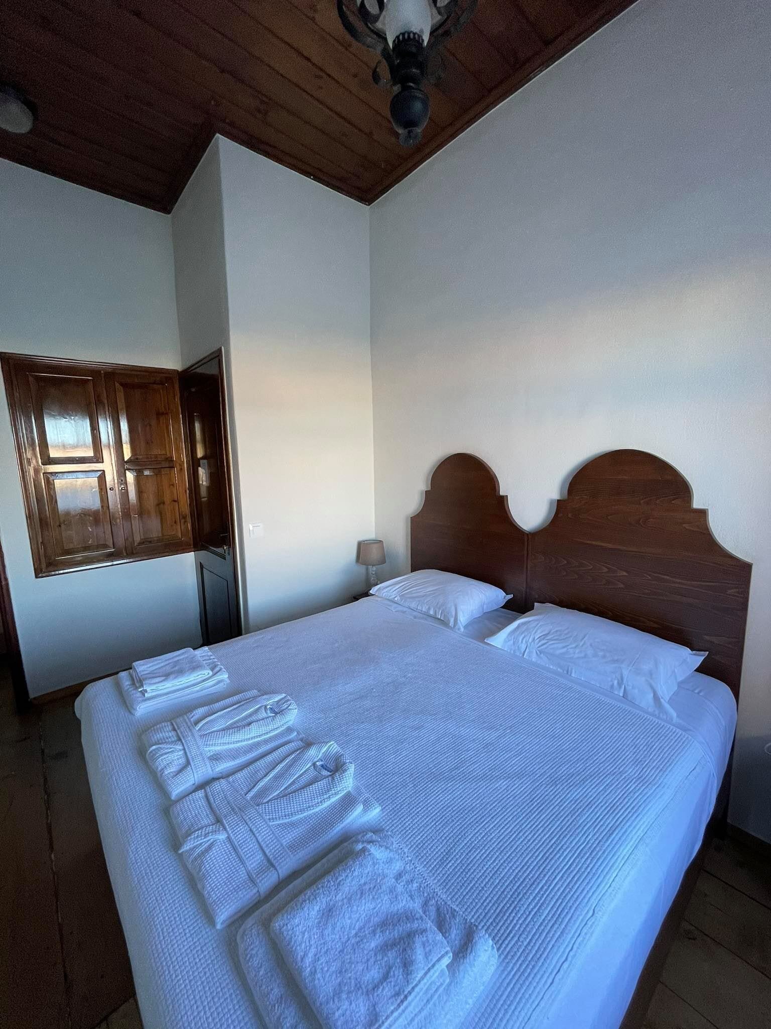 A hotel room with a large bed, wooden headboard, and neatly folded towels on the bed.