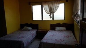 A room with two single beds, a window with curtains, a nightstand, and a view of the sea. - Hotel Posada Tayazal (Flores)