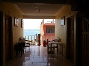A corridor with two wooden chairs and a small table, leading to a balcony with a view of the sea. - Hotel Posada Tayazal (Flores)