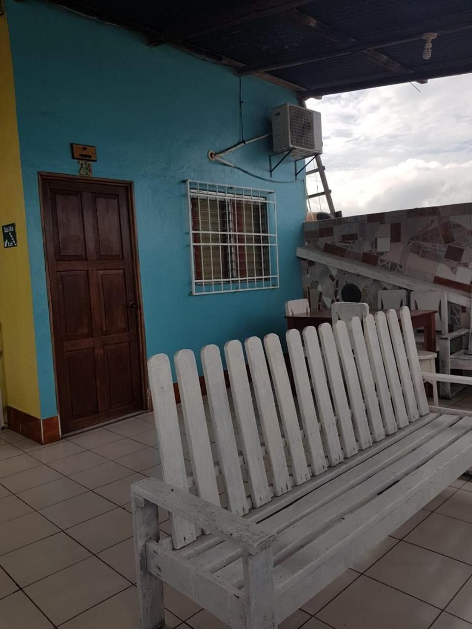 A bench outside a building with a blue wall, a door, and an air conditioning unit.