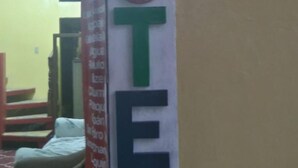 A hotel entrance with a sign reading "HOTEL" and a partial view of a room with a bed and a red chair. - Hotel Posada Tayazal (Flores)