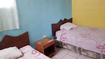 A small, simple room with two beds, a nightstand, and a window with a sheer curtain.