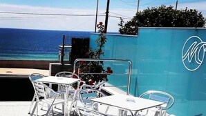 Un área de estar al aire libre con mesas y sillas de metal, con vista a un cuerpo de agua.