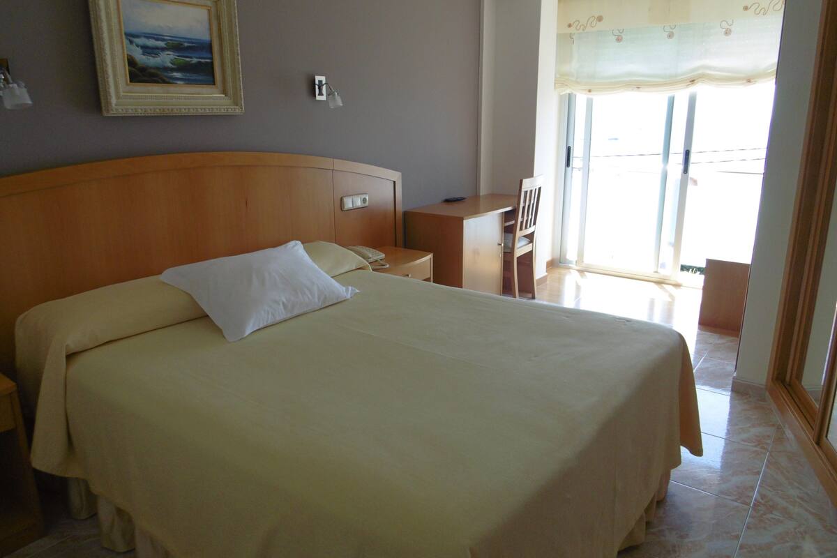 A neatly made bed with a pillow and a bedside table with a lamp.