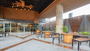 An outdoor seating area with wooden tables and benches, a central planter, and a modern architectural design with exposed beams and a concrete pillar. - EcoLoft Hotel (Phuket)