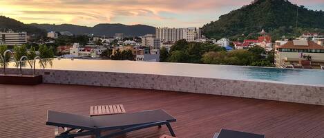 A rooftop terrace with wooden flooring, two lounge chairs, and a pool.