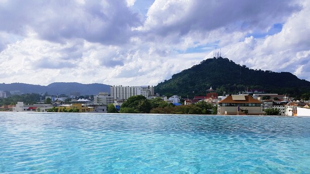 A swimming pool with clear water, buildings in the background, and a hill. - EcoLoft Hotel (Phuket)