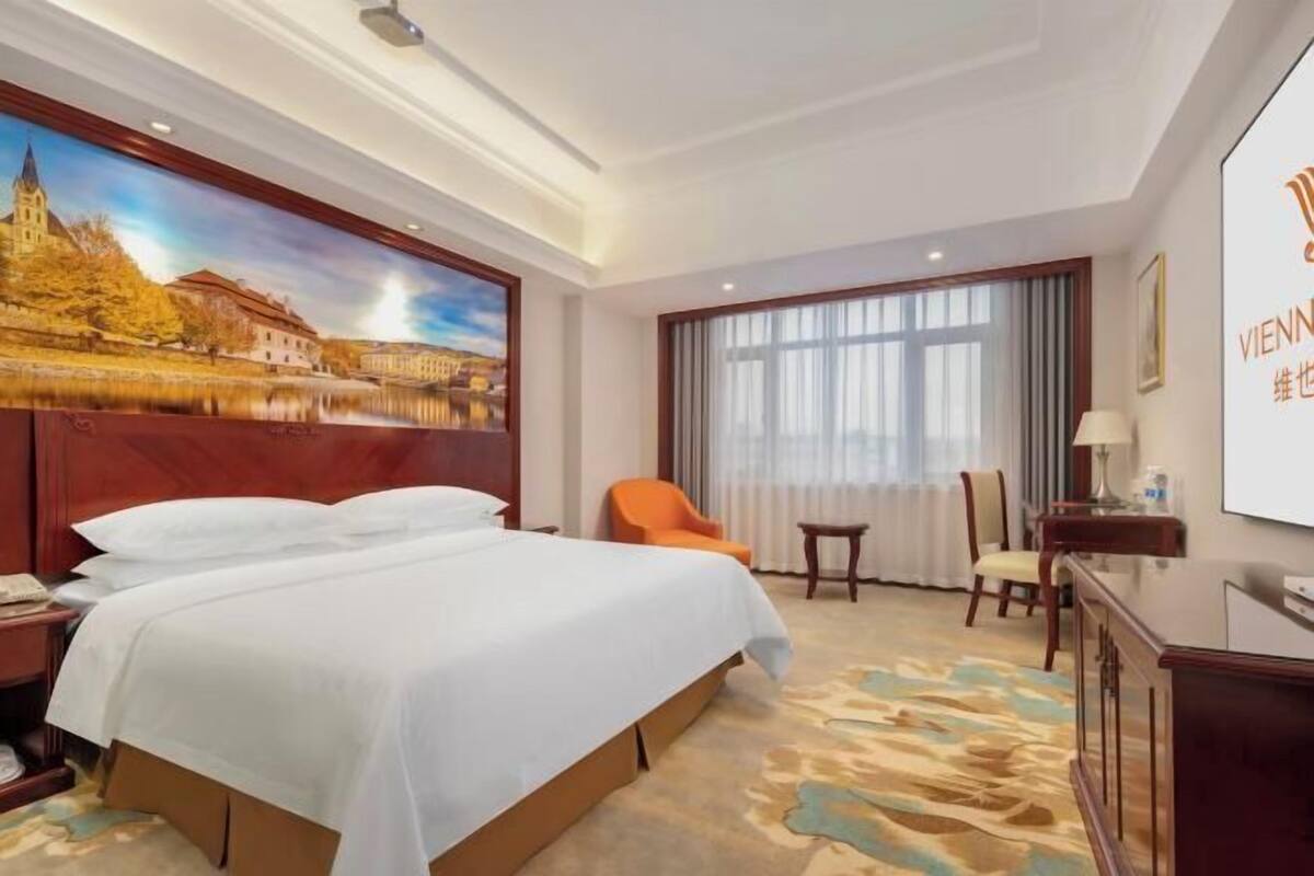 Une chambre d’hôtel avec un grand lit, un tableau représentant un paysage, un bureau et une chaise.