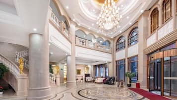 A grand lobby with a central circular floor design, large chandeliers, and a staircase with ornate details.