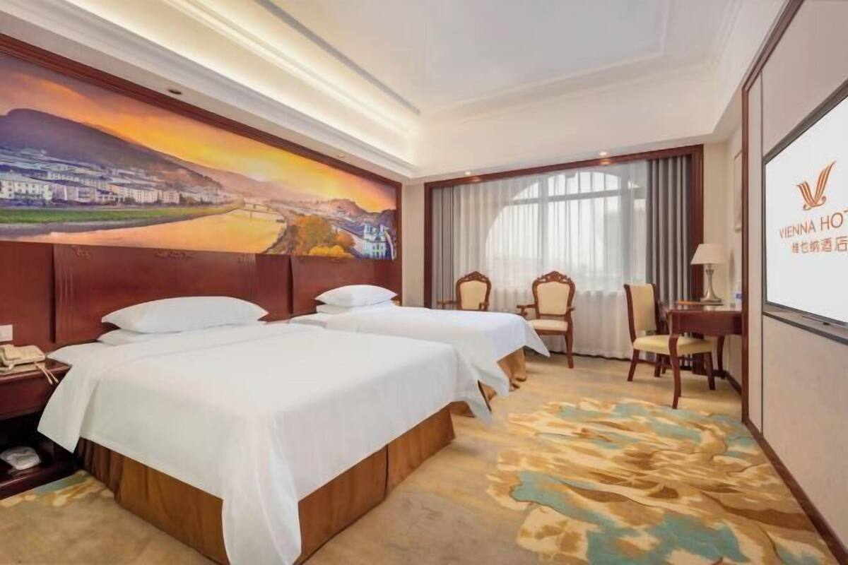 Une chambre d’hôtel avec deux lits, un bureau, une chaise et une grande fenêtre.
