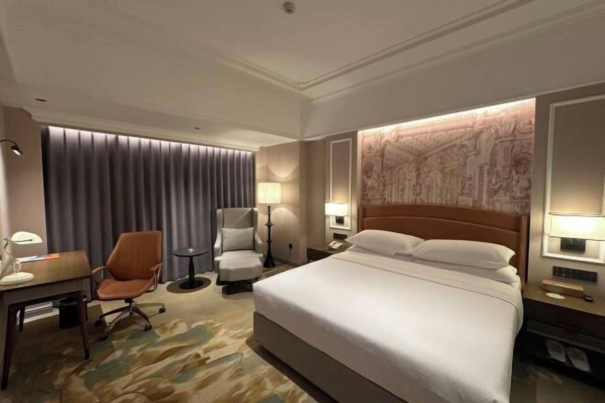 Une chambre d’hôtel avec un lit, un bureau, une chaise, une lampe et un mur orné d’une carte.