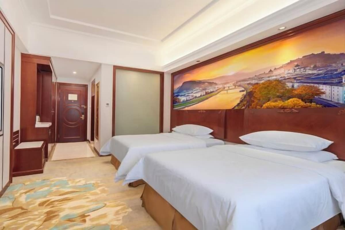 Quarto de hotel com duas camas, um grande mural na parede e piso coberto de carpete.