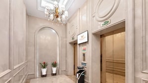 A hallway with a marble floor, a chandelier, potted plants, a reception desk, and a sign above a door. - Vienna Hotel (Ninghai) (Ninghai)
