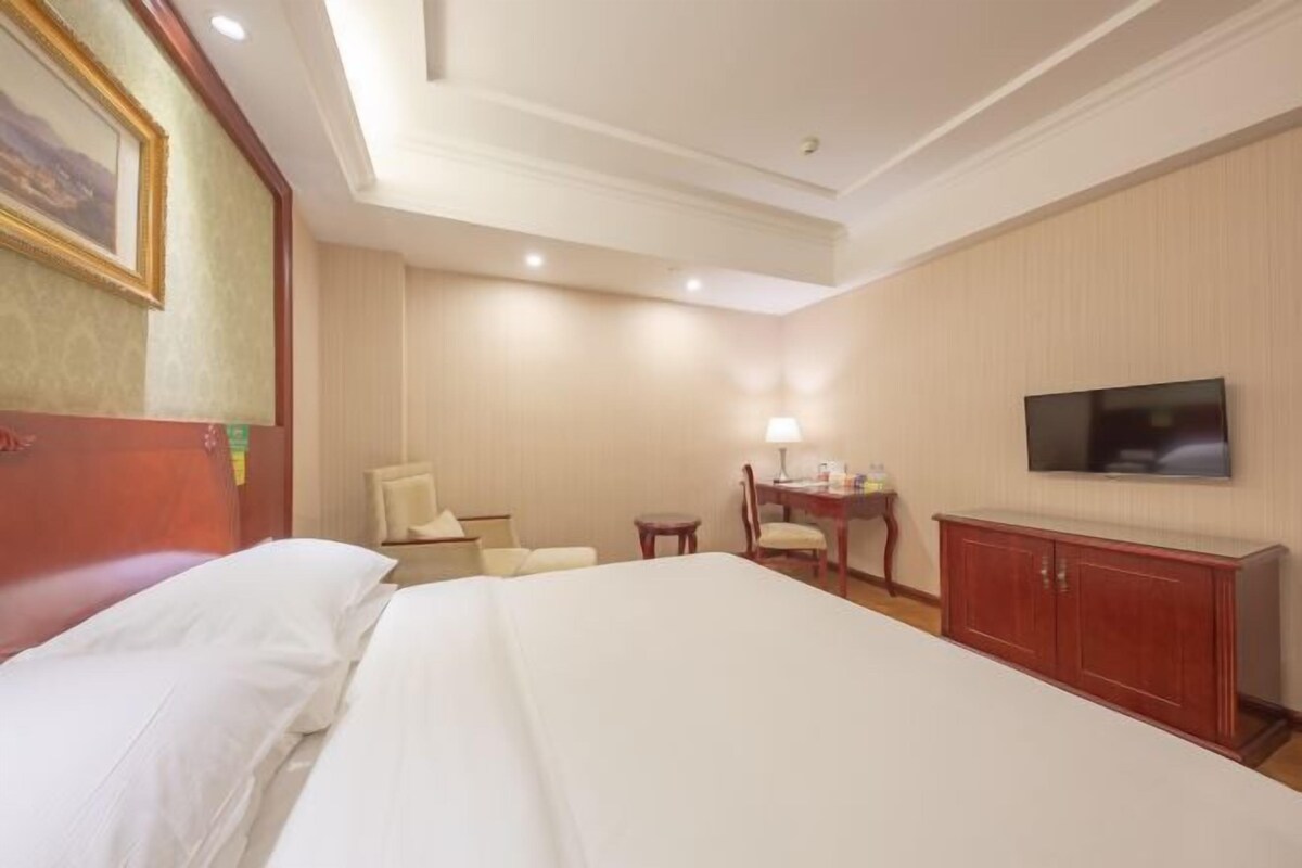 Quarto de hotel com uma cama grande, uma escrivaninha com cadeira, uma televisão e um armário.