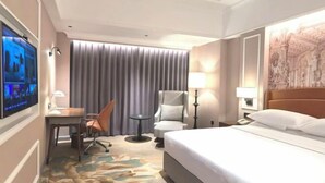 A hotel room with a large bed, a desk with a chair, a television, and a window with curtains.