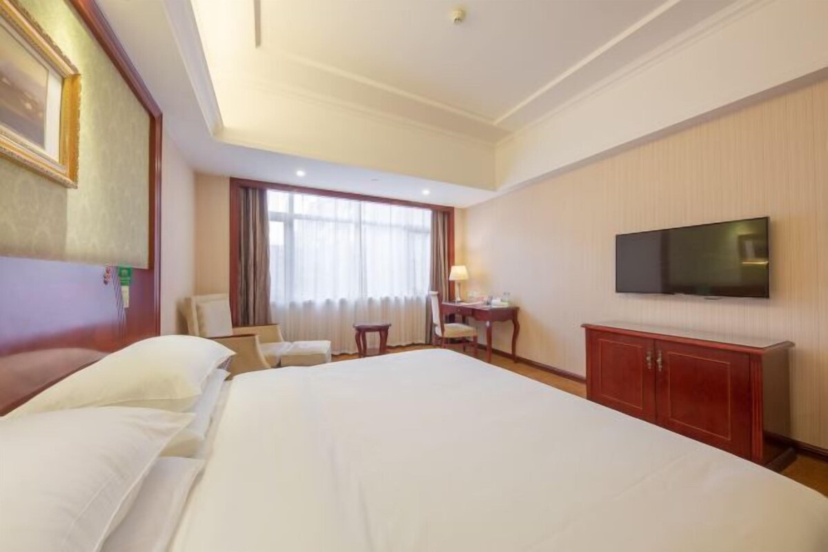 Quarto de hotel com uma cama grande, uma escrivaninha, uma cadeira, uma televisão e um guarda-roupa.