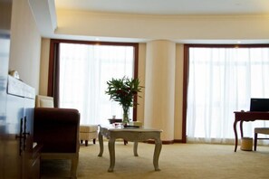 Quarto de hotel com uma janela grande, um sofá, uma mesa pequena e uma escrivaninha com um laptop.